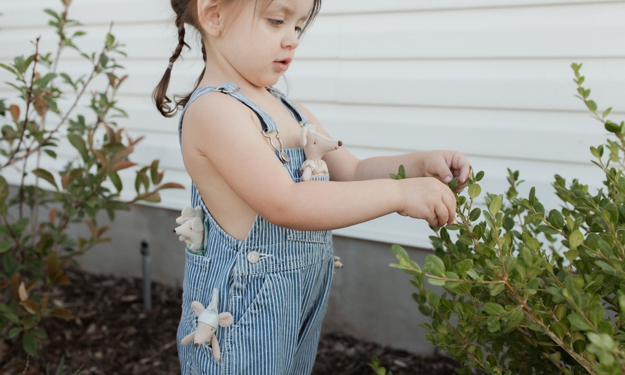 A child outside wearing overalls with Maileg mice in her pockets.