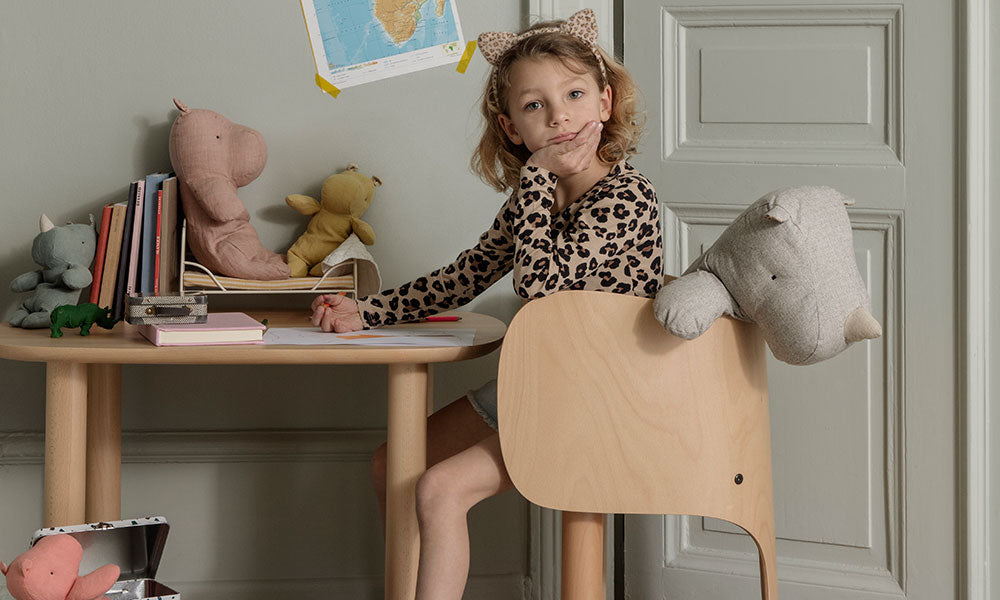 A girl sitting in a desk chair with Maileg Safari Friends