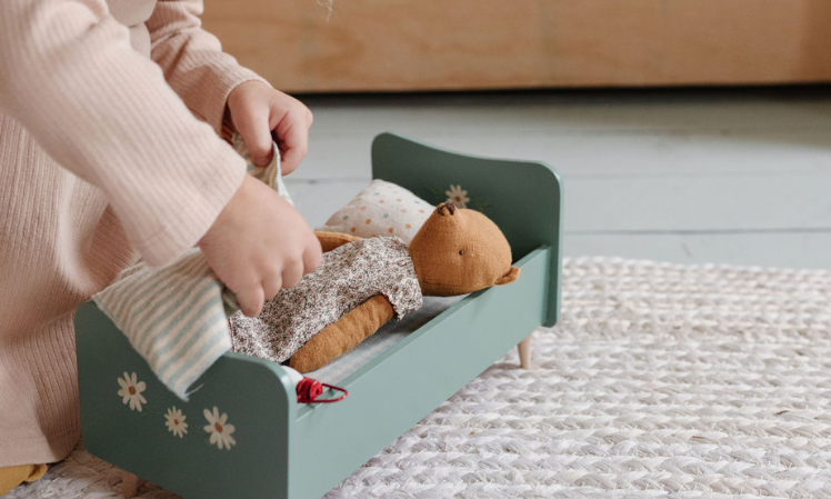 child tucking teddy mum into wooden bed